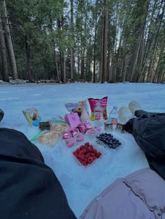 two people laying in the snow with food and snacks on their feet next to them