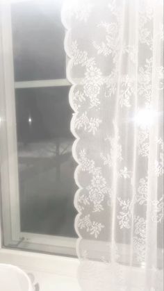 a window with white lace on it in front of a sink
