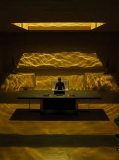 a man sitting at a desk in front of a wall with light coming through it