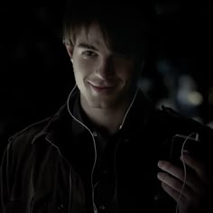 a young man is smiling and listening to music on his headphones in the dark