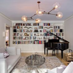 a living room filled with lots of furniture and a grand piano in front of a bookshelf