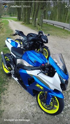 a blue and white motorcycle parked on the side of a dirt road next to trees