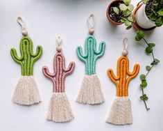 three cactus shaped key chains with tassels on top of them next to potted plants