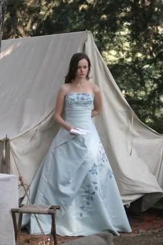 a woman in a blue dress standing next to a tent