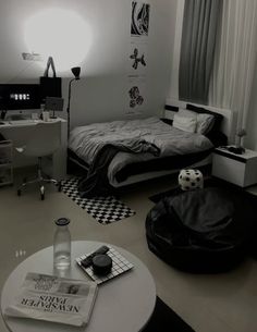 a black and white photo of a bedroom with a bed, desk, chair, lamp and other items