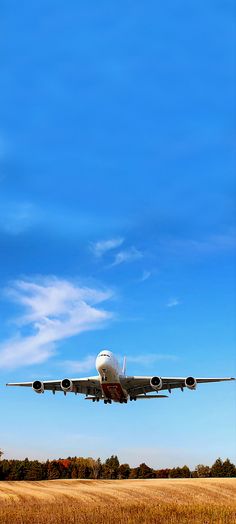 an airplane is flying low to the ground in front of a field and blue sky
