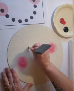a person is using a stamp on a paper plate with pink dots and black circles
