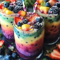 two glasses filled with fruit and topped with strawberries, blueberries, raspberries, and pineapples