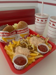 a tray filled with fries and french fries next to two cups of soda on a table