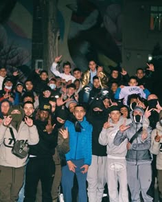 a group of young men standing next to each other in front of a building with their hands up
