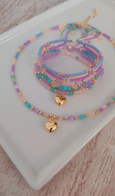 three bracelets with gold heart charms on a white plate next to a pink and blue beaded necklace