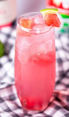 a close up of a drink in a glass on a checkered table cloth with limes and watermelon