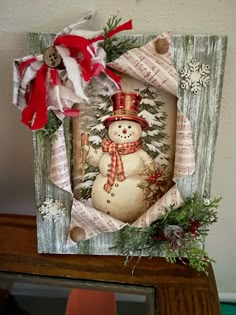 a snowman with a red hat and scarf hanging from a wooden frame on top of a table
