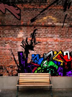 a wooden bench sitting in front of a brick wall with graffitti on it