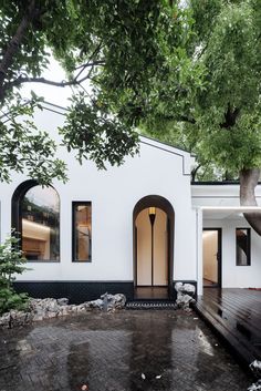 a white house with black trim and arched windows on the front door is surrounded by trees
