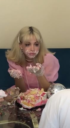a woman sitting at a table with cake on her face and confetti all over her mouth