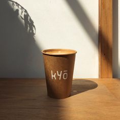 a brown cup sitting on top of a wooden table next to a planter with the word kyo written on it
