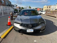 a silver acura is parked on the side of the road next to an orange cone
