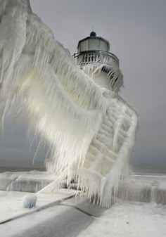 an ice covered lighthouse on the ocean with snow and icicles hanging from it's sides