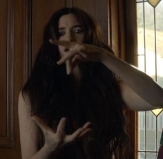 a woman with long dark hair is making a hand gesture in front of a stained glass window