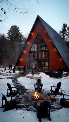a cabin in the woods is lit up with lights and chairs around an open fire pit