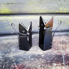 two metal cat sculptures sitting on top of a cement floor next to each other,
