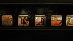 four people are sitting in the window of a train at night, with one person looking out