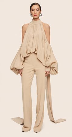 This flowing beige halter blouse features a gathered neckline and oversized draped sleeves for a bold statement. The fabric cascades elegantly down to tailored wide-leg trousers, creating a cohesive and polished silhouette. Ideal for fashion trends 2025, this look is perfect for sophisticated outfits women over 40. Latest Fashion Outfits, Women Outfits Aesthetic Summer, Top With Trousers Outfit, Dramatic Tops For Women, Bold Chic Fashion, Oversized Shirt Fashion, Chic Beige Top For Spring, Blouses 2025, Beige Clothing