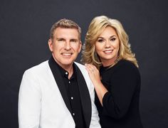 a man and woman posing for a photo in front of a black background with one arm around the other's shoulder