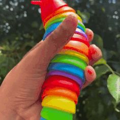 a hand holding a colorful toy in front of trees