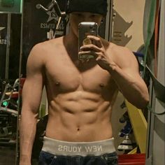 a shirtless man taking a selfie in the mirror with his cell phone and hat on