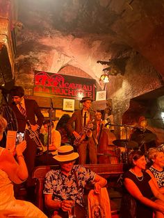 a group of people sitting around each other in front of a bar playing instruments and singing