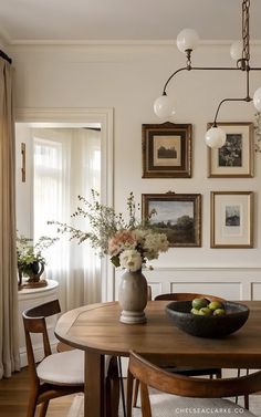 a dining room table and chairs with pictures on the wall above it, along with vases filled with flowers