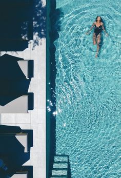 a woman is swimming in a pool with chairs and umbrellas on the sidelines