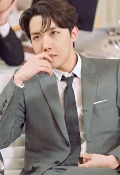 a young man in a suit sitting on a couch with his hand under his chin