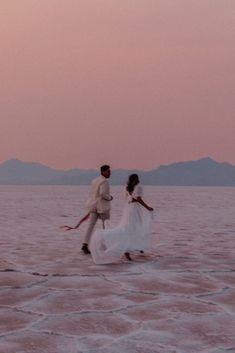 two people are walking across the water at sunset