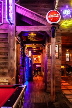 the inside of a bar with neon lights and pool tables in front of wooden walls
