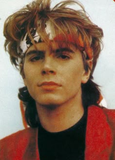 the young man is wearing a red jacket and has his hair pulled back into a pony tail