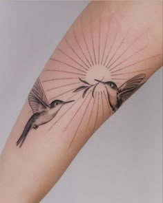 two birds flying in the air with sunbursts above them on a woman's arm