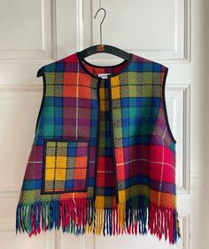 a multicolored plaid vest hanging on a white door with a wooden hanger