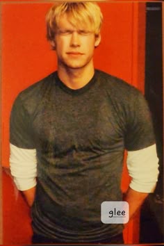 a young man standing in front of a red wall with his hands on his hips