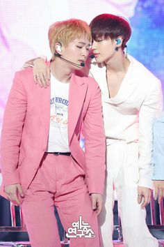 two men in pink suits and white shirts are kissing each other while one man is wearing headphones