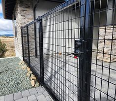 a black gate that is next to a brick wall and stone walkway with rocks on the ground