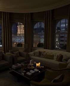 a living room with couches, chairs and tables in front of two large windows