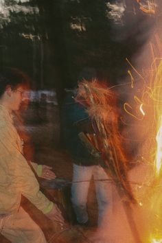 two men standing next to each other in front of a campfire with bright yellow flames