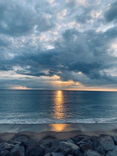 the sun is setting over the ocean with rocks on the shore and water in the foreground
