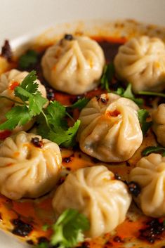 some dumplings are sitting on a plate with sauce and garnished green leaves