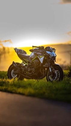 a motorcycle parked on the side of a road near some grass and trees at sunset