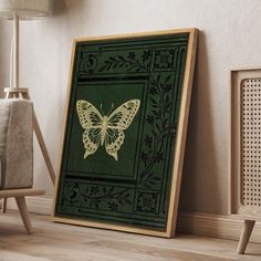 a green and gold framed art print with a butterfly in the center on a wood floor