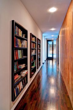 a long hallway with bookshelves and wooden floors on both sides is lit by recessed lights